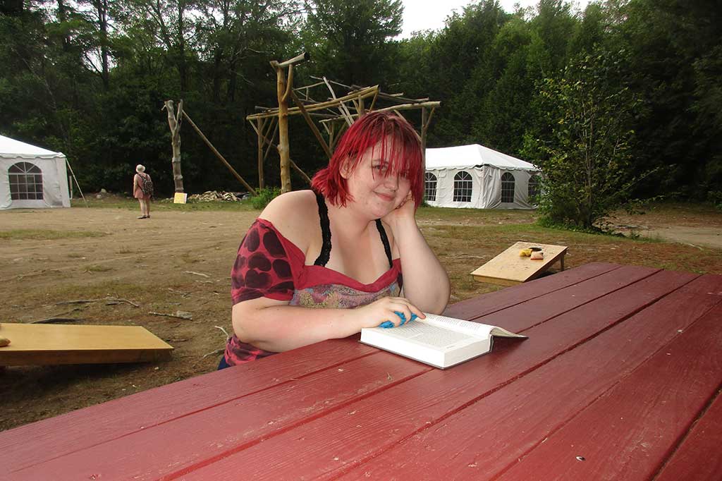 Teen sits at picnic table reading with smile.