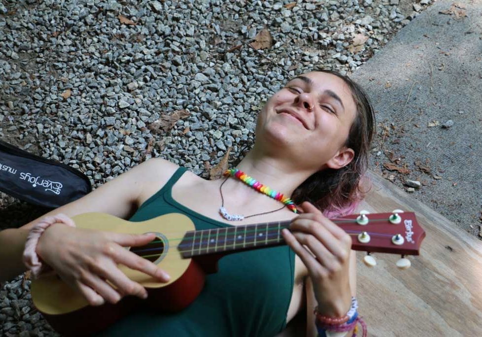 Camper lying on ground smiling and playing ukulele