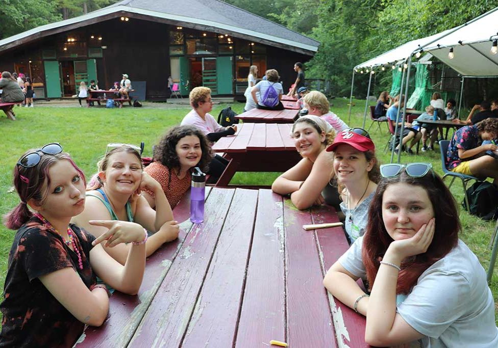 A group of teen campers eating lunch at a picnic table.