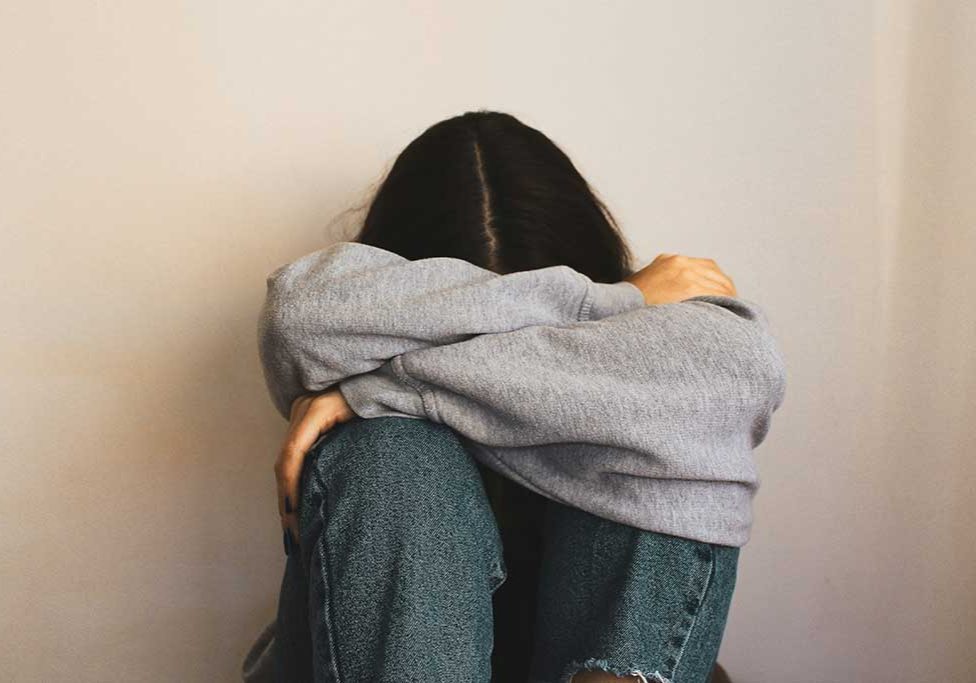 Teen with head down in lap sitting against wall.